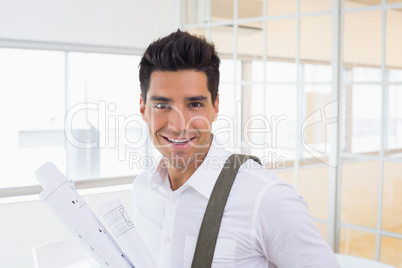 Casual handsome architect smiling at camera holding blueprint