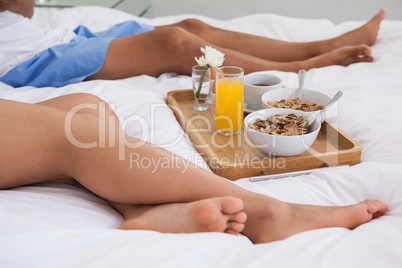 Couple lying on bed with breakfast on a tray