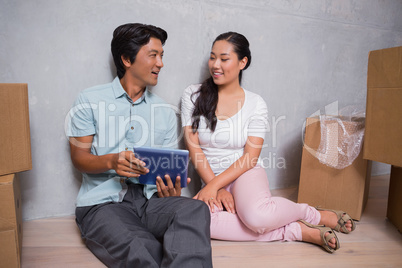 Happy couple sitting on floor using tablet surrounded by boxes