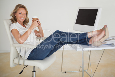 Casual businesswoman having a coffee with her feet up at desk