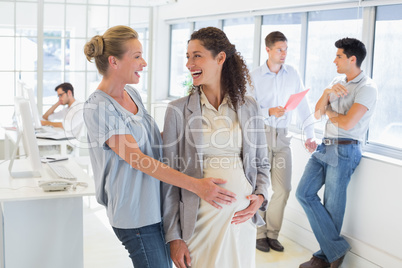 Casual businesswoman touching her pregnant colleagues belly