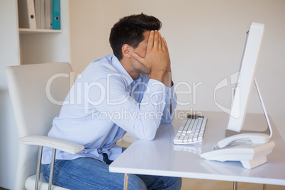 Casual businessman sitting at desk with head in hands