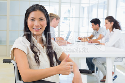 Casual businesswoman in wheelchair smiling at camera giving thum