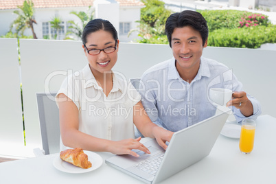 Smiling couple having breakfast together using laptop