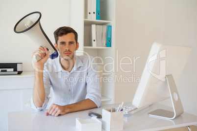 Casual businessman sitting at desk with megaphone