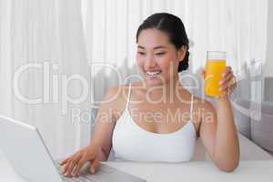 Happy woman using laptop and having orange juice