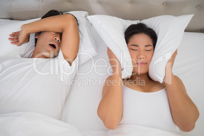 Annoyed woman covering her ears with pillows to block out snorin