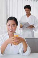 Woman in bathrobe having orange juice with boyfriend in backgrou