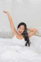 Smiling woman stretching in bed in the morning