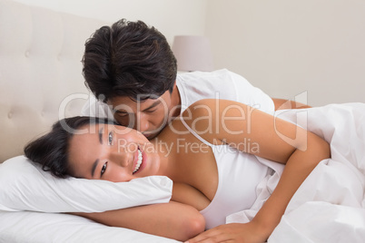 Man kissing his girlfriend on the cheek in bed