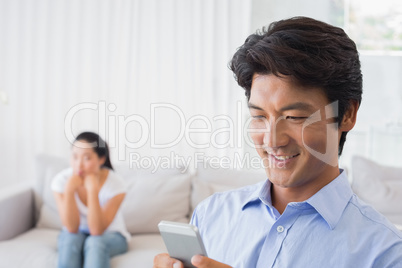 Man sending a text while girlfriend watches from couch