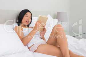 Smiling woman lying on bed reading