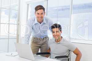 Casual businessman in wheelchair working at his desk with collea