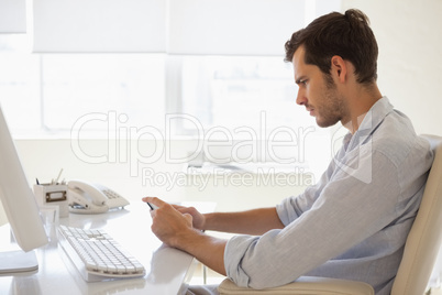 Casual businessman sending a text at his desk