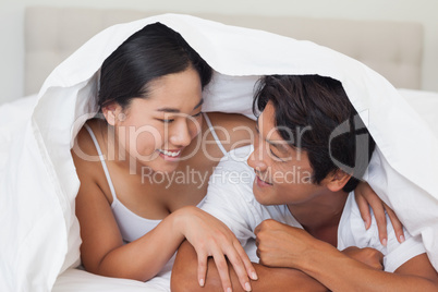 Happy couple lying on bed together under the duvet