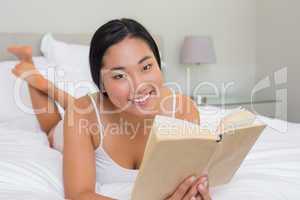 Smiling woman lying on bed reading