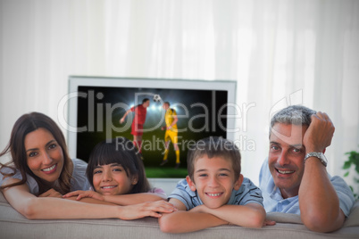 Family smiling at the camera with world cup showing on televisio