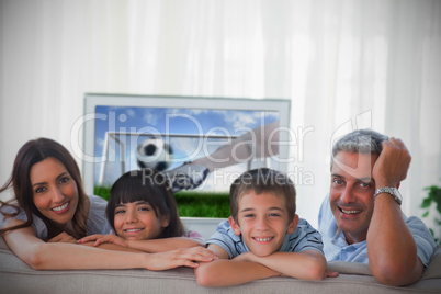 Family smiling at the camera with world cup showing on televisio