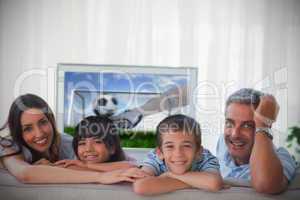 Family smiling at the camera with world cup showing on televisio