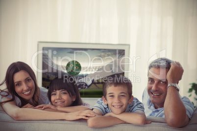 Family smiling at the camera with world cup showing on televisio