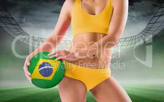 Composite image of fit girl in yellow bikini holding brazil football