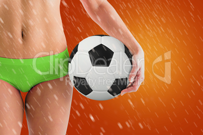 Composite image of fit girl in green bikini holding football