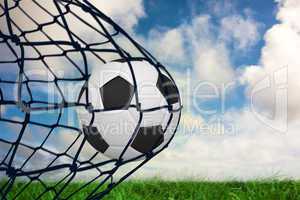 Composite image of football in back of the net