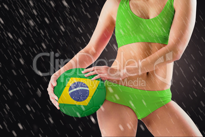 Composite image of fit girl in green bikini holding brasil ball