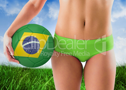 Composite image of fit girl in green bikini holding brazil footb