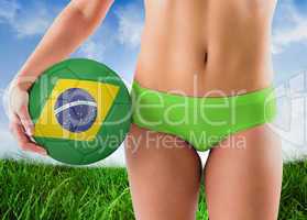 Composite image of fit girl in green bikini holding brazil footb