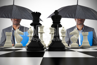 Composite image of businessman standing under umbrella with ches