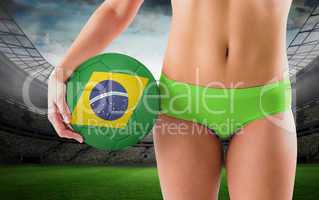 Composite image of fit girl in green bikini holding brazil football
