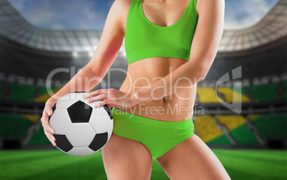 Composite image of fit girl in green bikini holding football