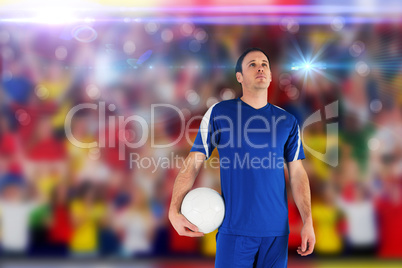 Composite image of handsome football player holding the ball