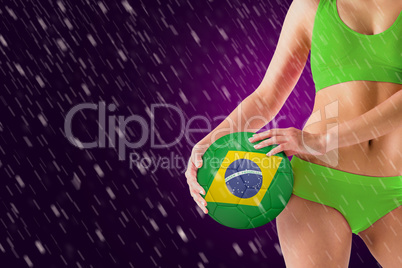 Composite image of fit girl in green bikini holding brasil ball