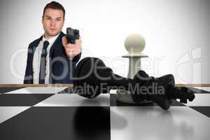 Composite image of serious businessman pointing a gun at chess p
