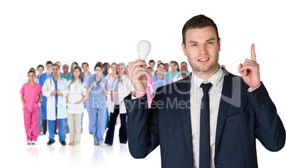 Composite image of businessman holding light bulb and pointing