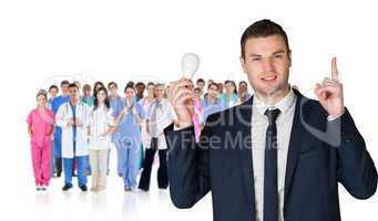 Composite image of businessman holding light bulb and pointing