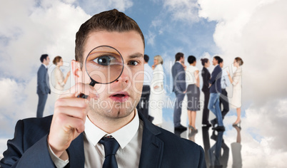 Composite image of businessman looking through magnifying glass