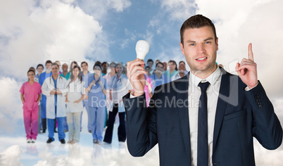 Composite image of businessman holding light bulb and pointing