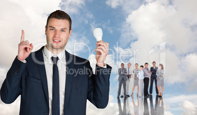 Composite image of businessman holding light bulb and pointing