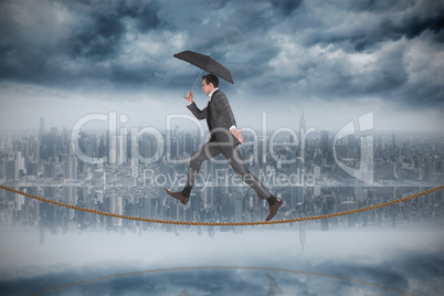 Composite image of businessman jumping holding an umbrella on ti
