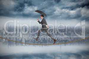 Composite image of businessman jumping holding an umbrella on ti