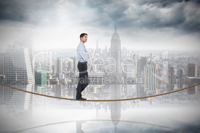 Composite image of serious asian businessman on tightrope