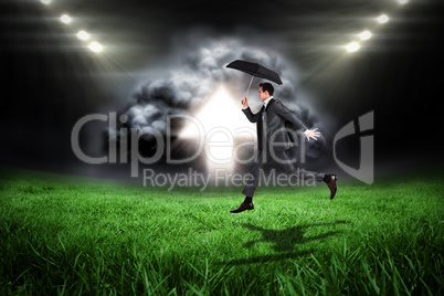 Composite image of businessman jumping holding an umbrella