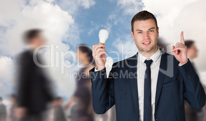 Composite image of businessman holding light bulb and pointing