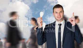 Composite image of businessman holding light bulb and pointing