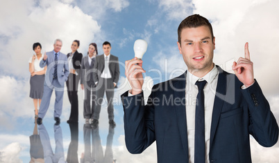 Composite image of businessman holding light bulb and pointing