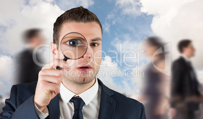 Composite image of businessman looking through magnifying glass