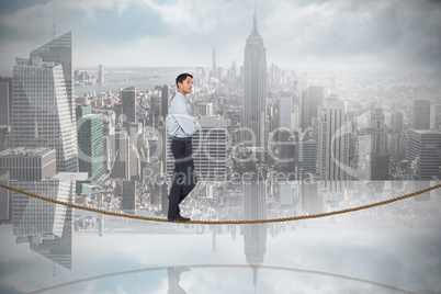 Composite image of serious asian businessman on tightrope